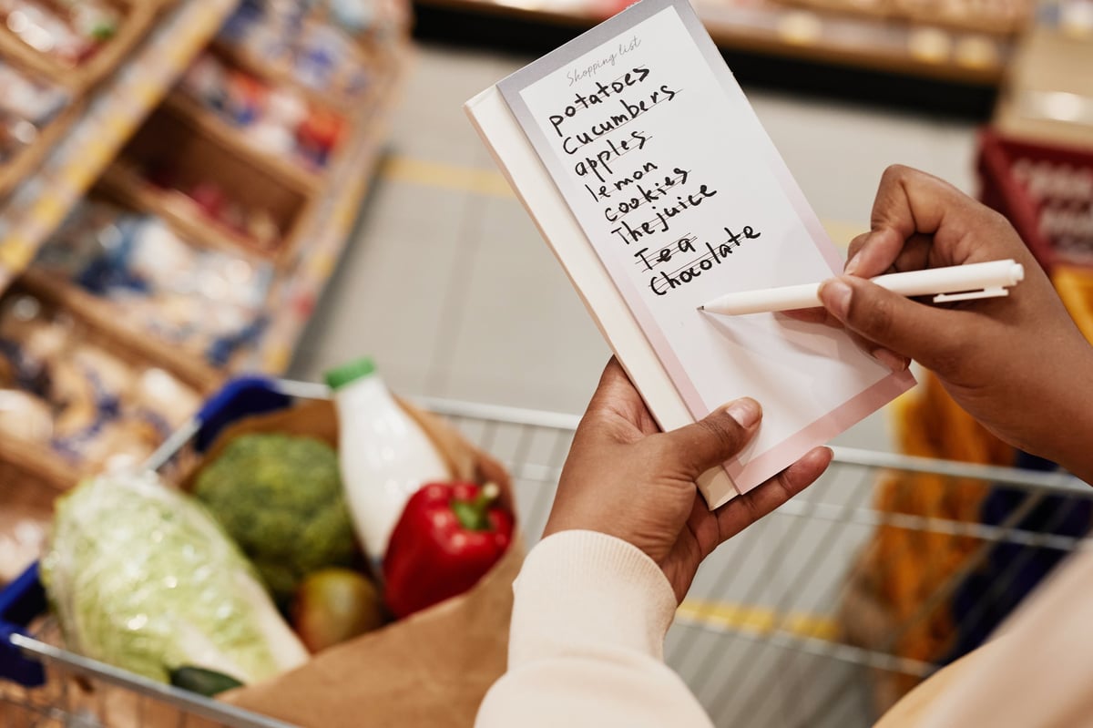 Shopper holding a Grocery LISS list while selecting food in a supermarket