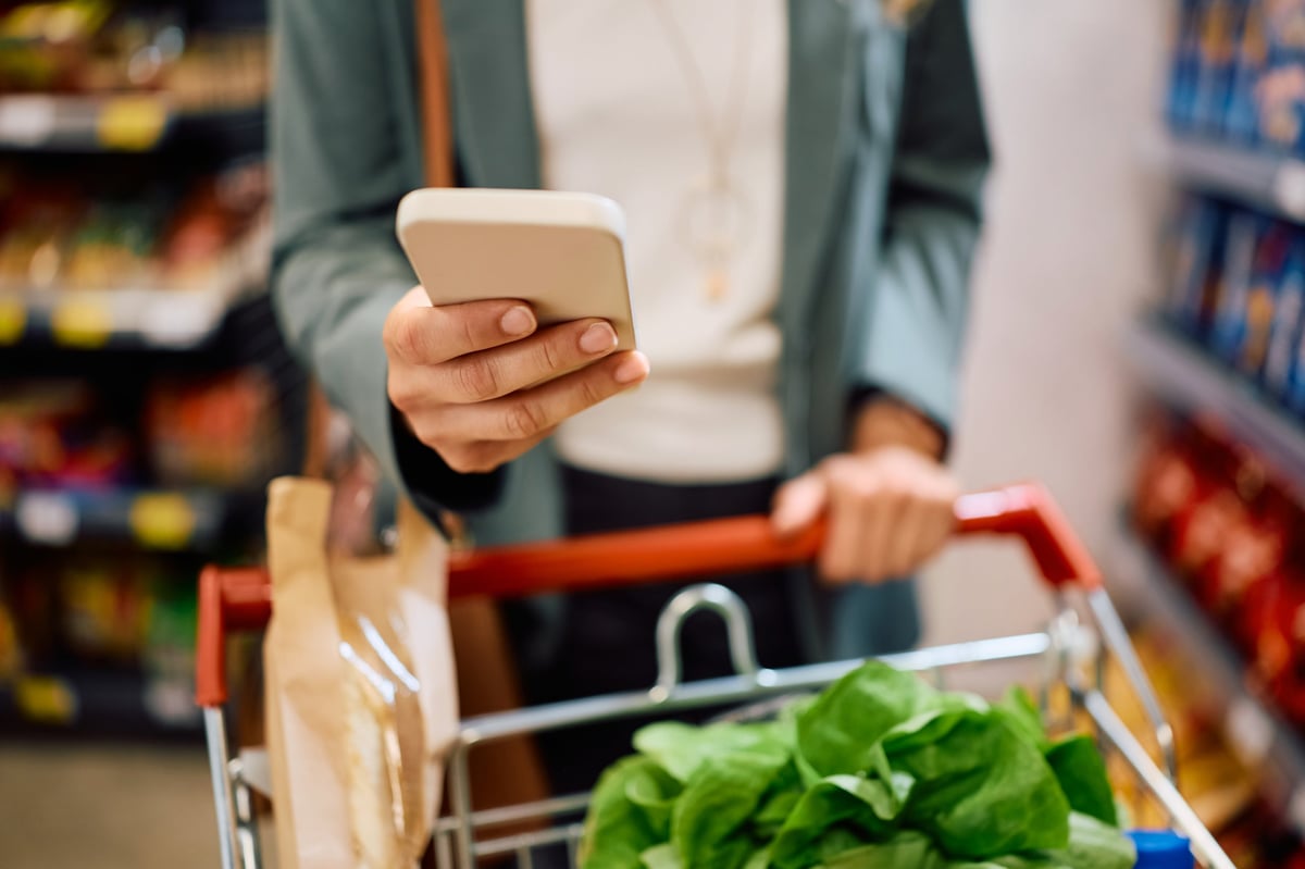 Woman using the Grocery LISS app on her phone while shopping in a supermarket